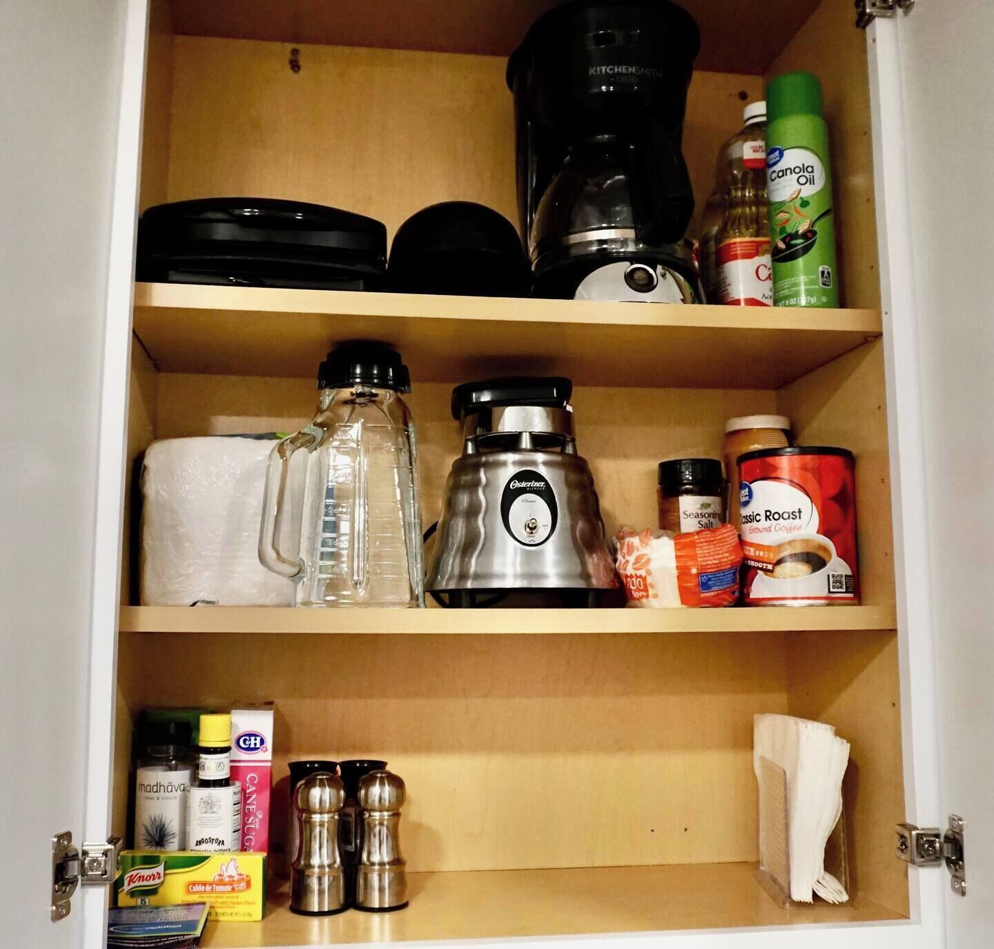 Una dispensa con scaffali contenenti diversi oggetti, come una macchina per il caffè, olio di colza, sale aromatico e chicchi di caffè.