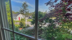 A view through a window with a metal screen, displaying a residential area with houses, trees, and a clear sky. - Open Hearth Inn Suite 2 - 10 min to Acadia! (Trenton)
