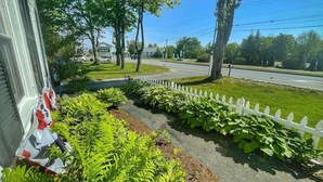 A residential street with a white picket fence, lush green plants, and a clear blue sky. - Open Hearth Inn Suite 2 - 10 min to Acadia! (Trenton)
