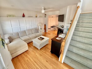 A spacious living room with a sofa, coffee table, and a fireplace. A staircase is visible to the right.
