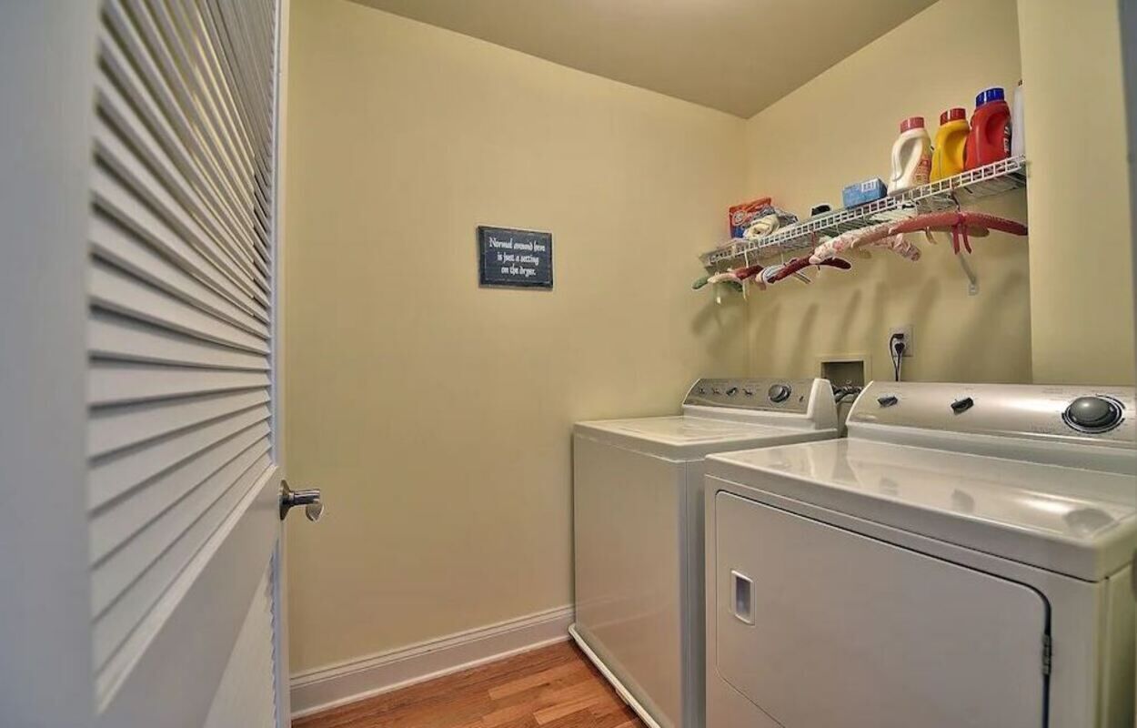A laundry room with a washing machine and dryer, a shelf with cleaning supplies, and a sign on the wall.