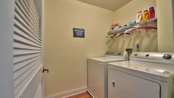A laundry room with a washing machine and dryer, a shelf with cleaning supplies, and a sign on the wall.