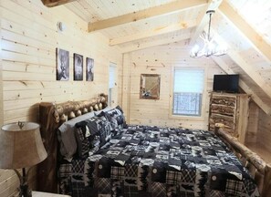 Un dormitorio rústico de cabaña de troncos con cama, lámpara, televisor y ventana.