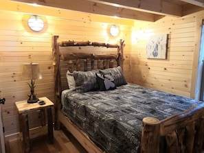 A wooden cabin bedroom with a bed, a nightstand, and a lamp. - Queen of Hearts. Secluded Hocking Hills cabin. (Rockbridge)