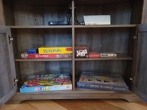 A wooden cabinet with four shelves, each holding a different board game.