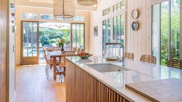 A modern kitchen with a large island, wooden flooring, and large windows offering a view of the outdoors.