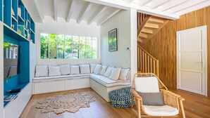 A modern living room with a built-in bench, a wicker chair, a large window, and a wooden staircase.