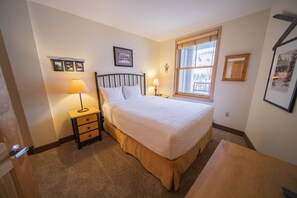 A bedroom with a bed, bedside tables, a lamp, a window with a view, and framed pictures on the wall. - Silver Mill 8262 (Keystone)