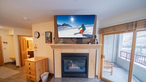Uma sala de estar com lareira, televisão montada acima dela e vista para uma paisagem nevada através de uma porta de correr.