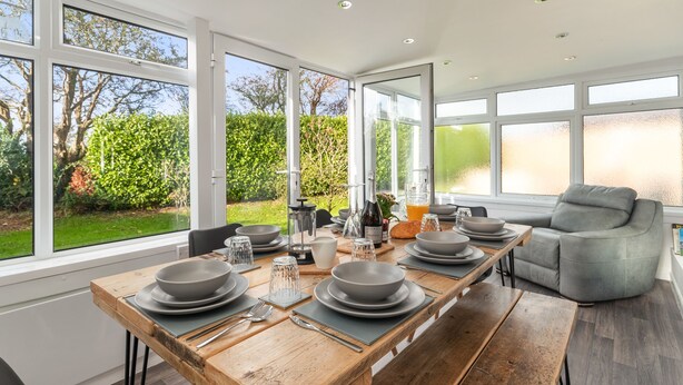 A modern kitchen with large windows, a dining table set for four, and a grey sofa. - Ty Gwyn - Hot Tub Parking Dog Friendly (Saundersfoot)