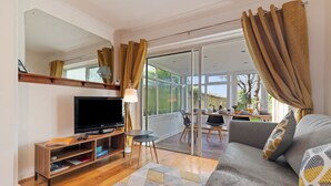 A modern living room with a flat-screen TV, wooden entertainment unit, sofa, and a dining area with a glass door leading to a balcony. - Ty Gwyn - Hot Tub Parking Dog Friendly (Saundersfoot)