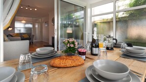 A dining area with a table set for breakfast, including plates, bowls, a loaf of bread, and a bottle of wine. - Ty Gwyn - Hot Tub Parking Dog Friendly (Saundersfoot)
