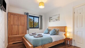 Une chambre à coucher avec un lit en bois, une armoire, une fenêtre avec des rideaux, une table de chevet avec une lampe et un tableau accroché au mur.