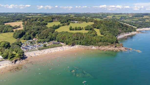 Une vue aérienne d’une zone côtière comprenant une plage, une zone boisée et un petit bâtiment surmonté d’un drapeau.