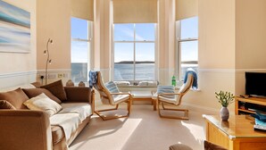 A living room with a beige sofa, two rocking chairs, a glass coffee table, and a TV stand.
