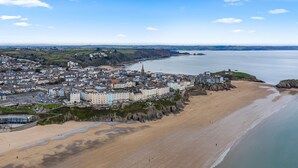 An aerial view of a coastal town with a sandy beach, a prominent church, and a castle on a hill.