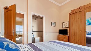 A bedroom with a bed, a wooden wardrobe, a television, and a bathroom visible through an open door.