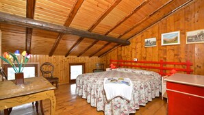 Um quarto de madeira com uma cama, uma mesa e um aparador vermelho.