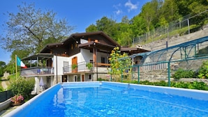 Vista da piscina de um chalé com varanda, uma bandeira e montanhas ao fundo.
