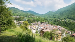 Uma vila na encosta com edifícios tradicionais, rodeada por montanhas verdes e árvores exuberantes.