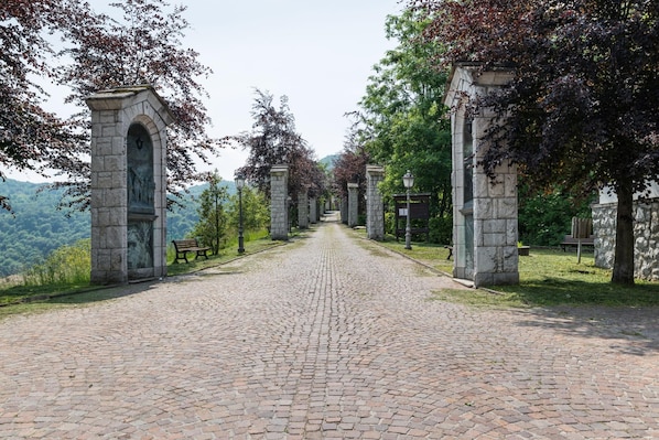 A cobblestone pathway leading to a stone archway with benches and lampposts.
