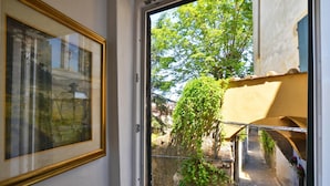 A window with a view of a narrow alleyway, a framed picture on the wall, and a building with a yellow facade. - Casina Magnoli (Florence)