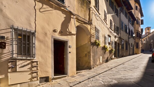 A narrow cobblestone street with buildings featuring arched doorways and barred windows. - Casina Magnoli (Florence)