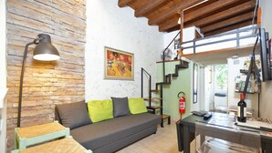 A cozy living room with a sofa, a table, and a lamp. There is a staircase leading to an upper level. - Casina Magnoli (Florence)