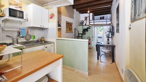 A compact kitchen with white cabinets, a microwave, and a stove. There is a small island with a sink and a stool. The kitchen has wooden flooring and a stone accent wall. - Casina Magnoli (Florence)