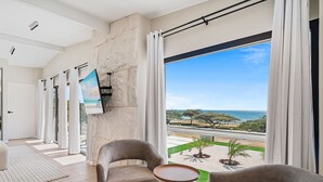 A modern room with a large window, a stone wall, and a view of a beach. - Massive Oceanfront Villa - Spa - Sauna - Gameroom - Malmok! (Noord)
