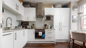 A modern kitchen with white cabinets, a stainless steel range hood, a microwave, and a wooden dining table. - Supreme Hampstead Home Next to Hampstead Heath by Underthedoormat (London)