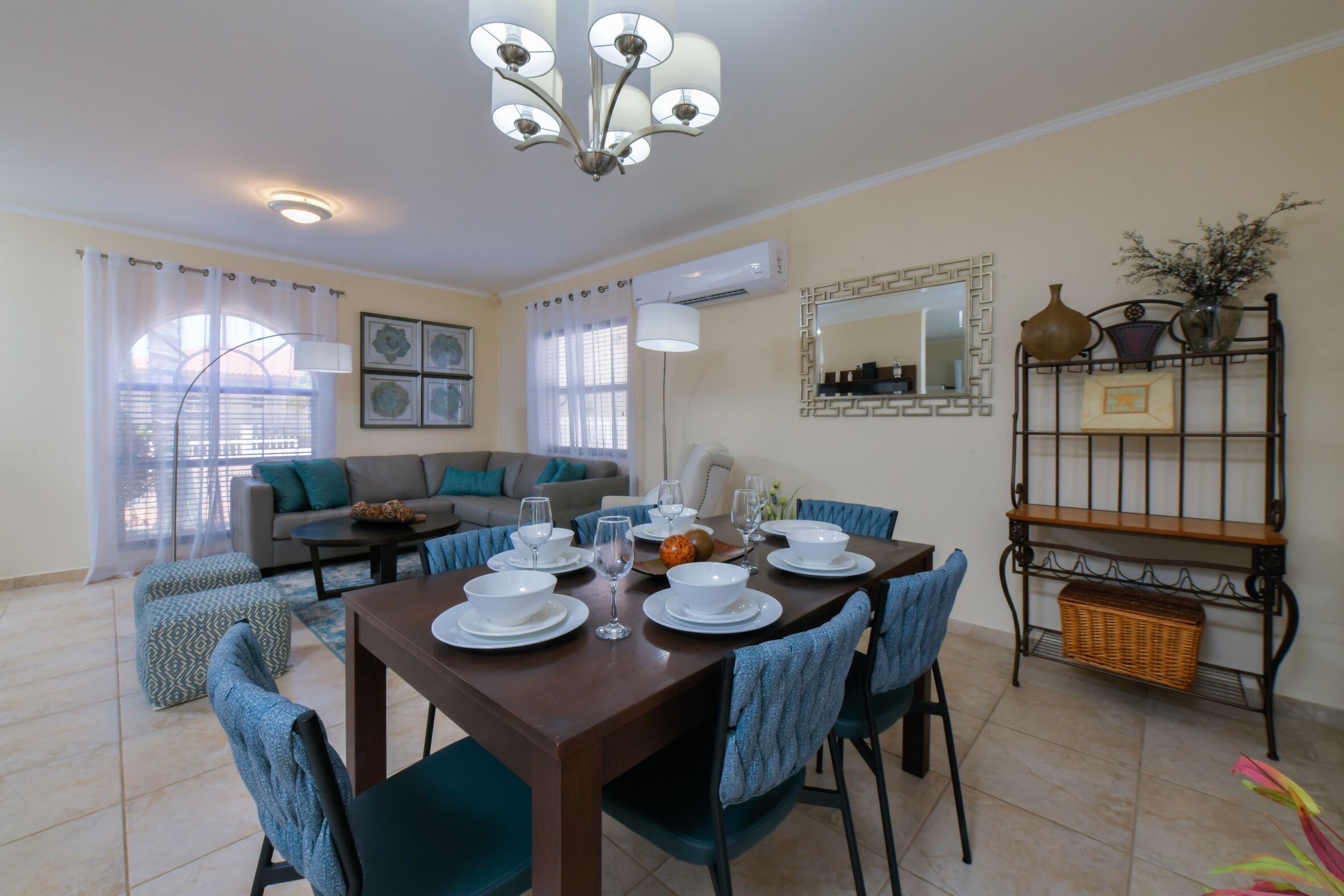 Un comedor con una mesa preparada para cuatro personas, rodeada de sillas. Se observa un sofá y una mesa de centro al fondo.