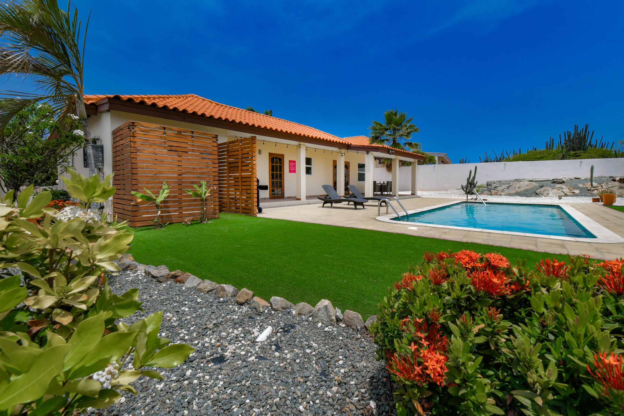 Una casa con piscina, patio con poltrone relax e prato ben curato.