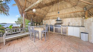 Una cocina exterior con techo de paja, una parrilla empotrada y encimera de piedra.