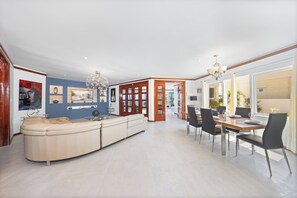 A modern living room with a beige sectional sofa, a dining area with a wooden table and chairs, and a chandelier. - Private Beach Ocean Front Boat Dock Tiki Bar (Savaneta)
