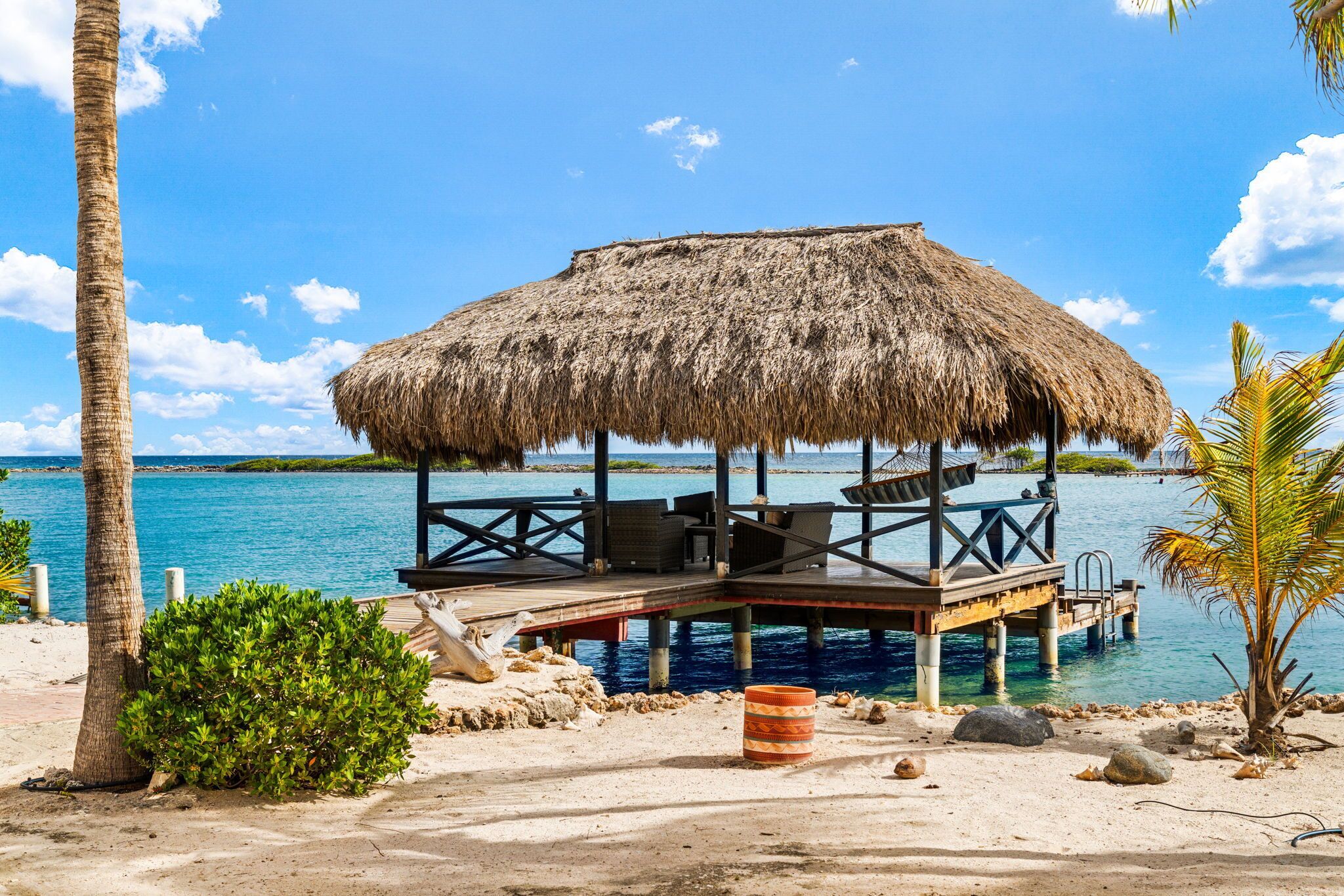A beachside structure with a thatched roof, wooden deck, and seating area.