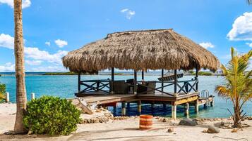 A beachside structure with a thatched roof, wooden deck, and seating area.