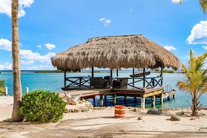 A beachside structure with a thatched roof, wooden deck, and seating area. - Private Beach Ocean Front Boat Dock Tiki Bar (Savaneta)