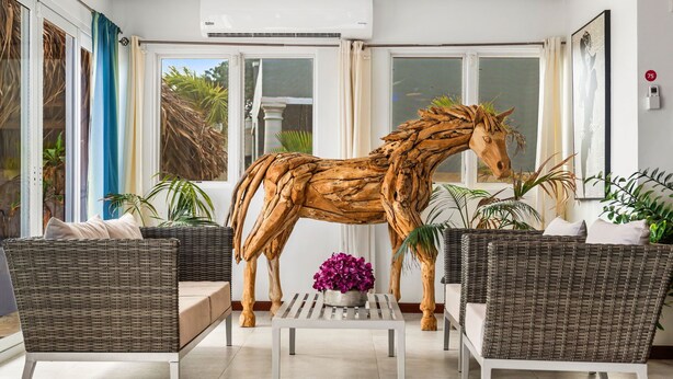 Una habitación con mobiliario de mimbre, una escultura de un caballo de madera y plantas en macetas.