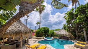 A pool area with lounge chairs, a hot tub, and thatched umbrellas. - Mexican Style Villa With Private Pool, Free Utilities (Oranjestad)
