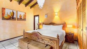 A bedroom with a wooden bed, a nightstand, a wall-mounted lamp, and two paintings of vases. - Mexican Style Villa With Private Pool, Free Utilities (Oranjestad)