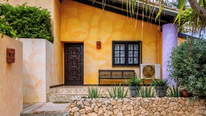 A building with a stone wall, a bench, and a door with a geometric pattern. - Mexican Style Villa With Private Pool, Free Utilities (Oranjestad)