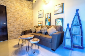A modern living room with a brick wall, a sofa with patterned cushions, a round coffee table, and a decorative ladder.