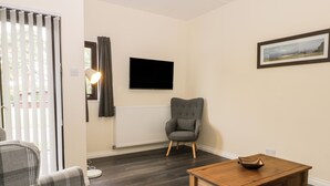 A living room with a plaid sofa, a grey armchair, a wooden coffee table, a flat-screen TV mounted on the wall, and a framed picture. - Lavender Lodge (Saltburn-by-the-Sea)