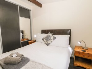 A neatly made bed with a patterned pillow, a bedside table with a lamp, and a wooden nightstand. - Lavender Lodge (Saltburn-by-the-Sea)