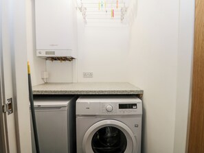 A compact laundry area with a washing machine and dryer, a small shelf with a power outlet, and a window with a drying rack. - Lavender Lodge (Saltburn-by-the-Sea)