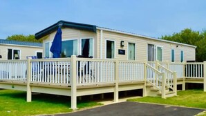 Une maison mobile dotée d’une terrasse, d’un espace extérieur couvert et d’un petit escalier menant à l’entrée.