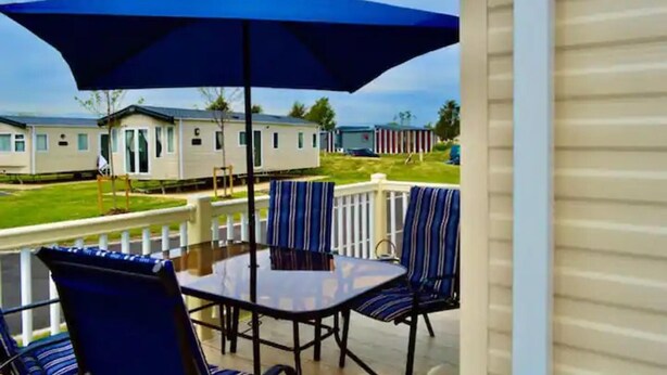 Une terrasse avec une table et des chaises, un parasol, et une vue sur des maisons mobiles en arrière-plan.