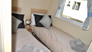 Un lit simple avec une tête de lit en bois, une table de chevet surmontée d’un globe terrestre et une fenêtre avec des rideaux.