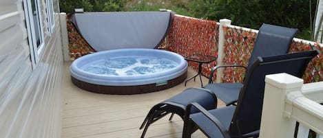 A hot tub on a wooden deck with two chairs, surrounded by a decorative fence.